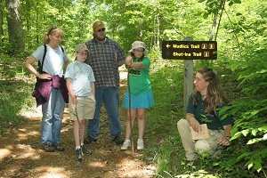 the park naturalist points out a plant on a guided hike with a family