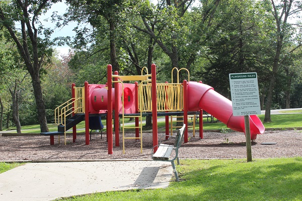 a bench sits near playground equipment with a few slides