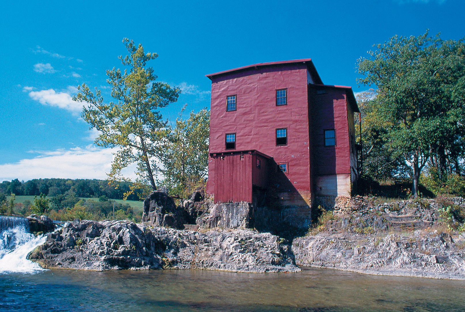 red mill with water cascading over a ledge next to it
