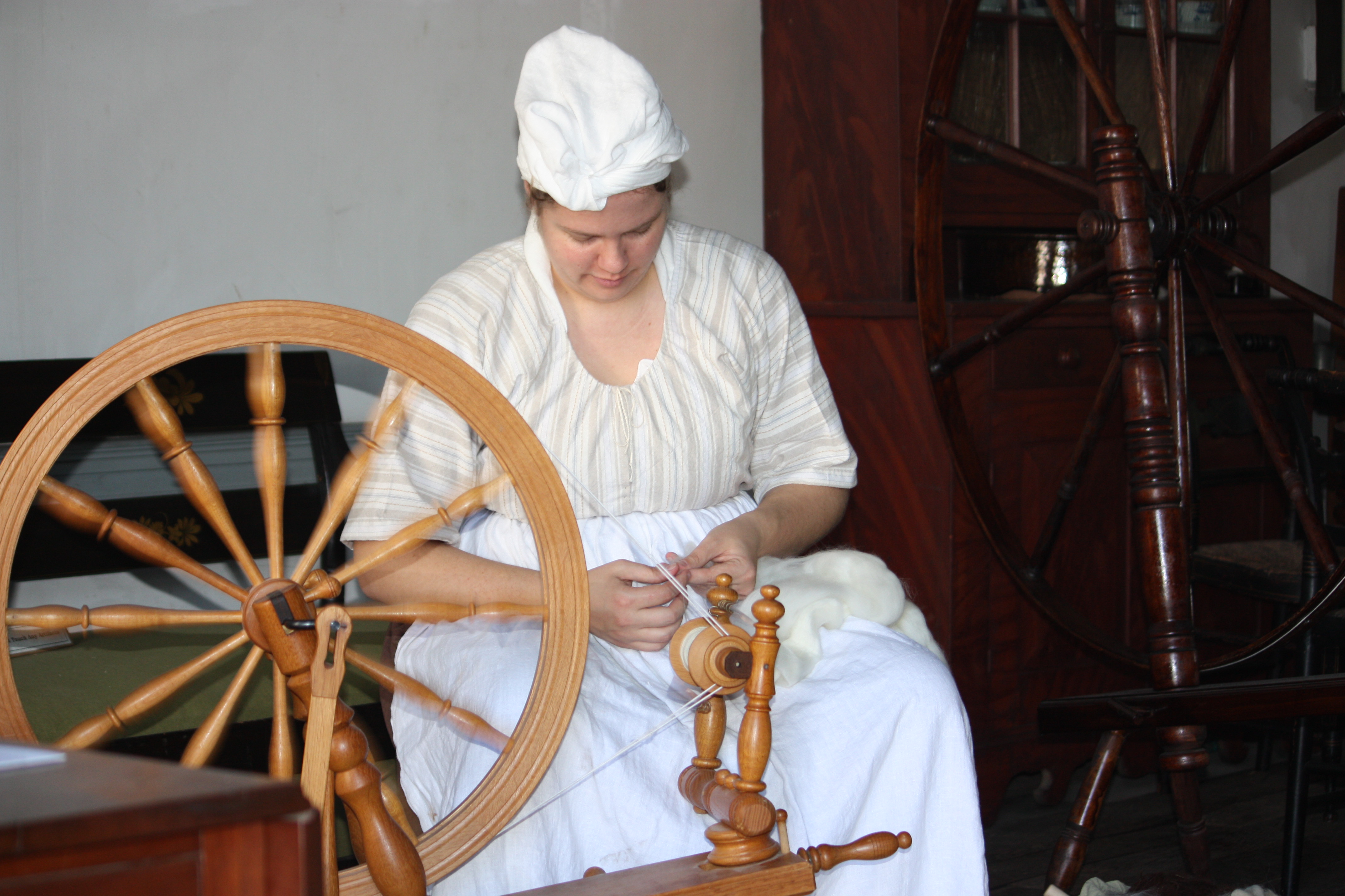 woman in period attire weaving with a spinning wheel