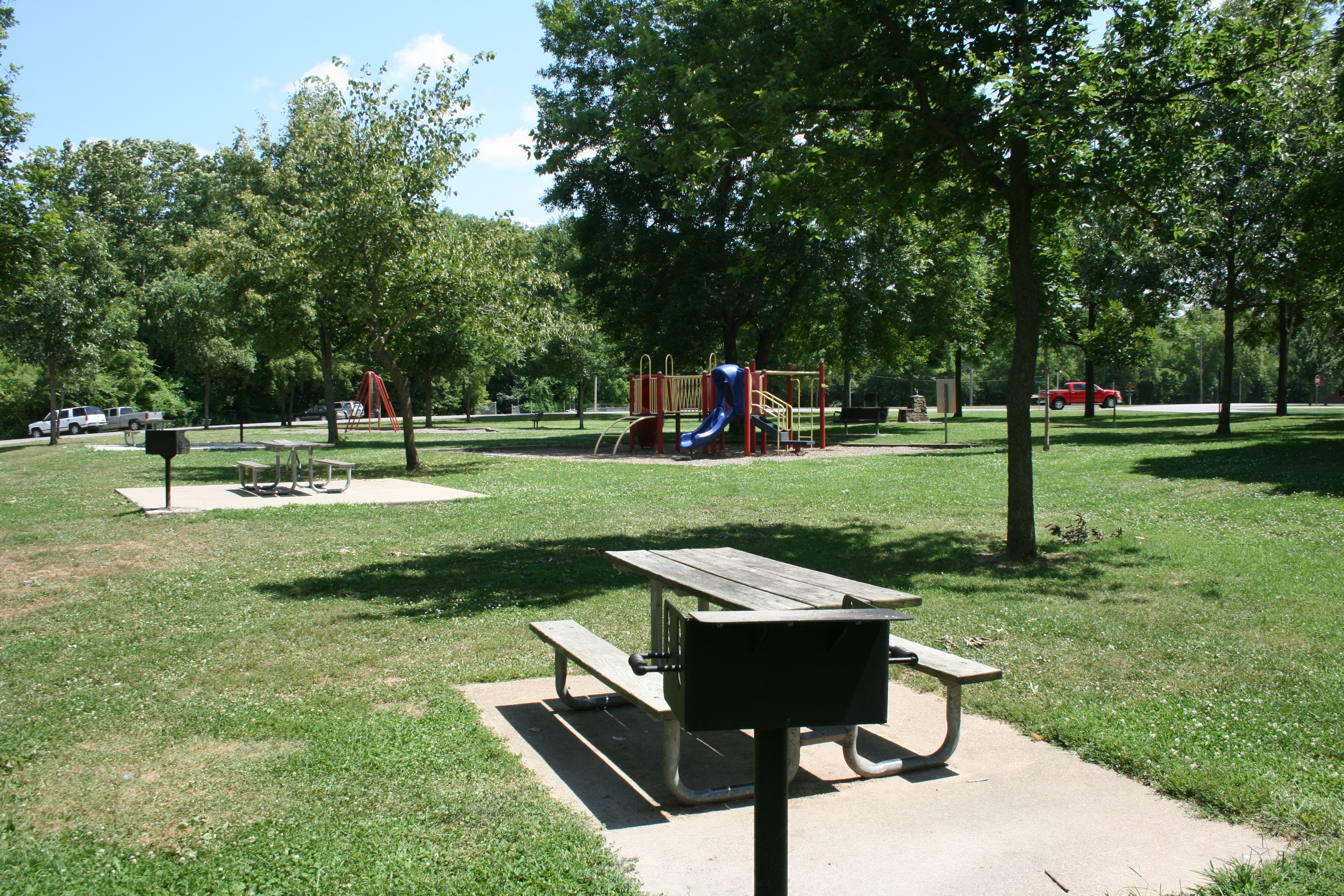 A sunny picnic area with scattered picnic tables with grills