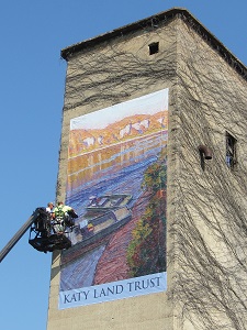 construction person on a lift puting up a Katy Land Trust banner