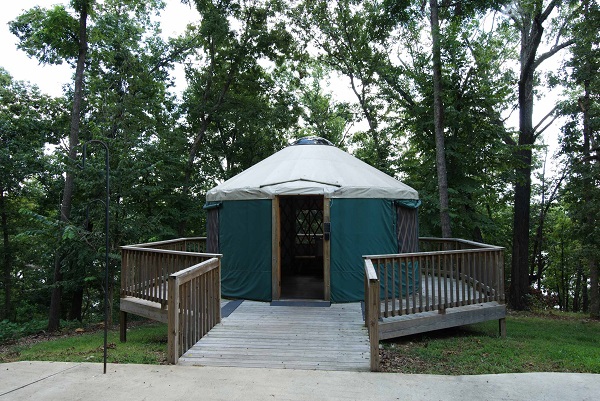 exterior of yurt with a deck beneath large shade trees