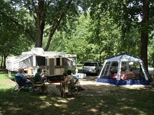people sitting at the campsite with a camper and tent behind them