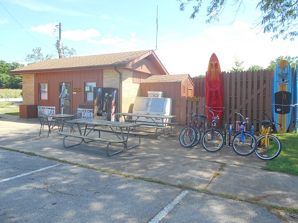 exterior of store with soda machine, ice, picnic tables, kayaks and bicycles in front