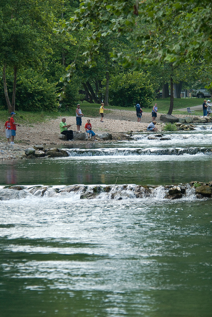 small cascades of water flowing down the river with people fishing on the bank