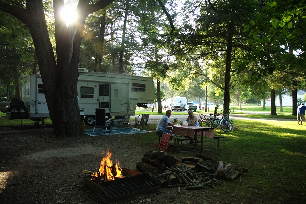 Couple sittling at picnic table in front of their camper with a campfire in the foreground