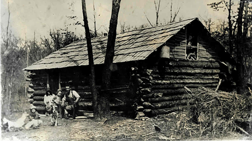 Black and white photo of family sitting outside a log cabin