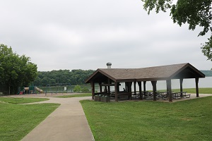 a sidewalk leads to the picnic shelter and playground next to the lake
