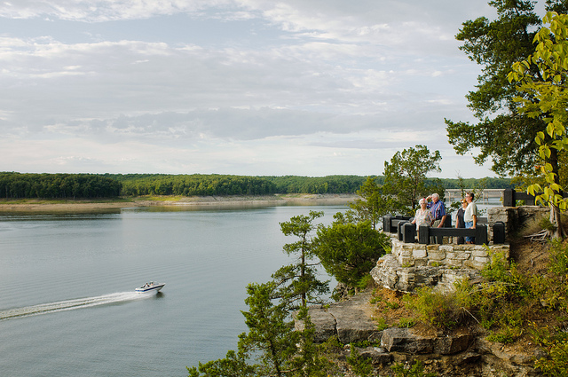 people standing on a rock overlook watching a boat go by on the lake below
