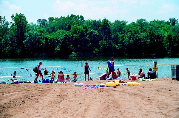 several people sitting on the beach and swimming in the lake