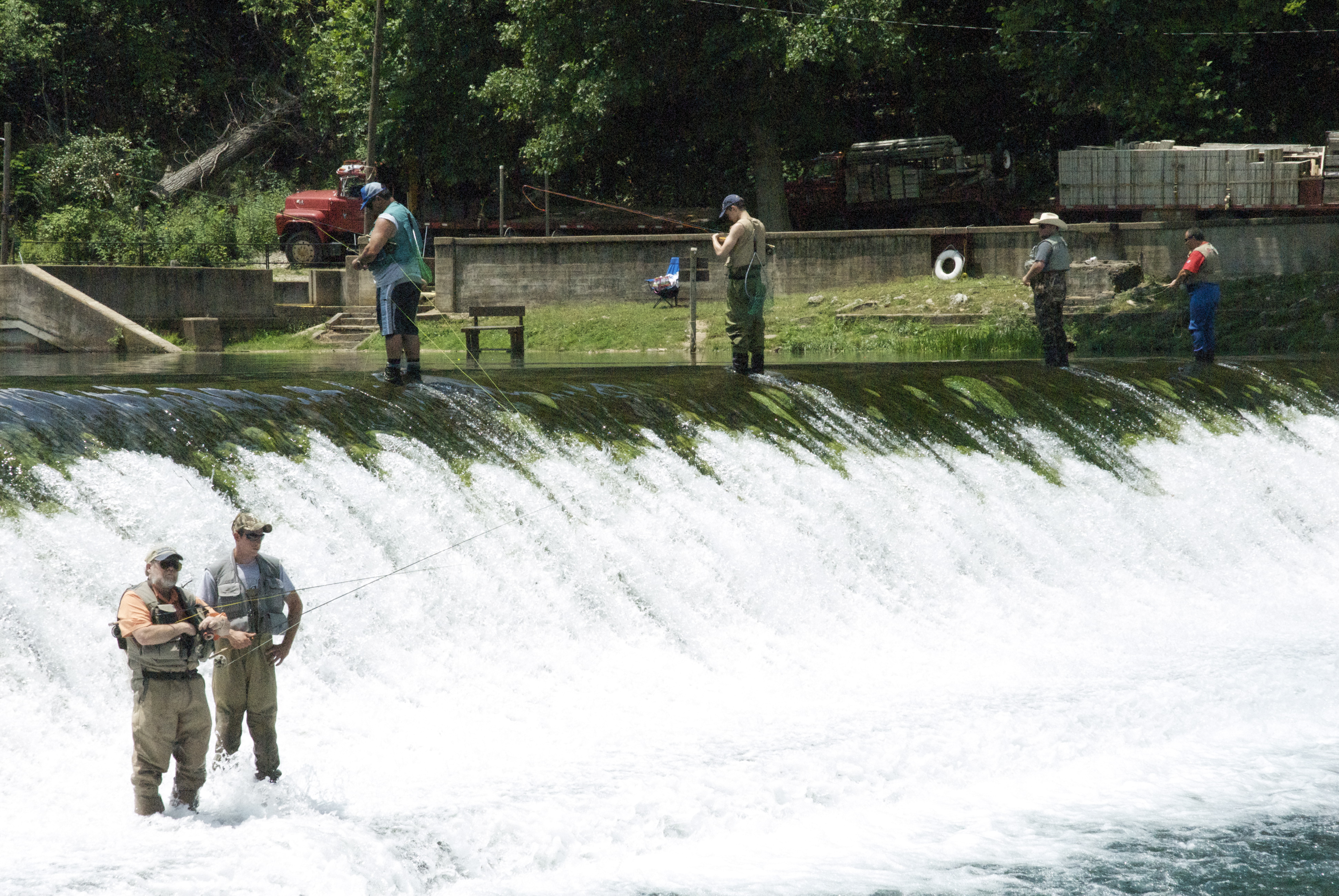 many people fishing standing on top of a short waterfall