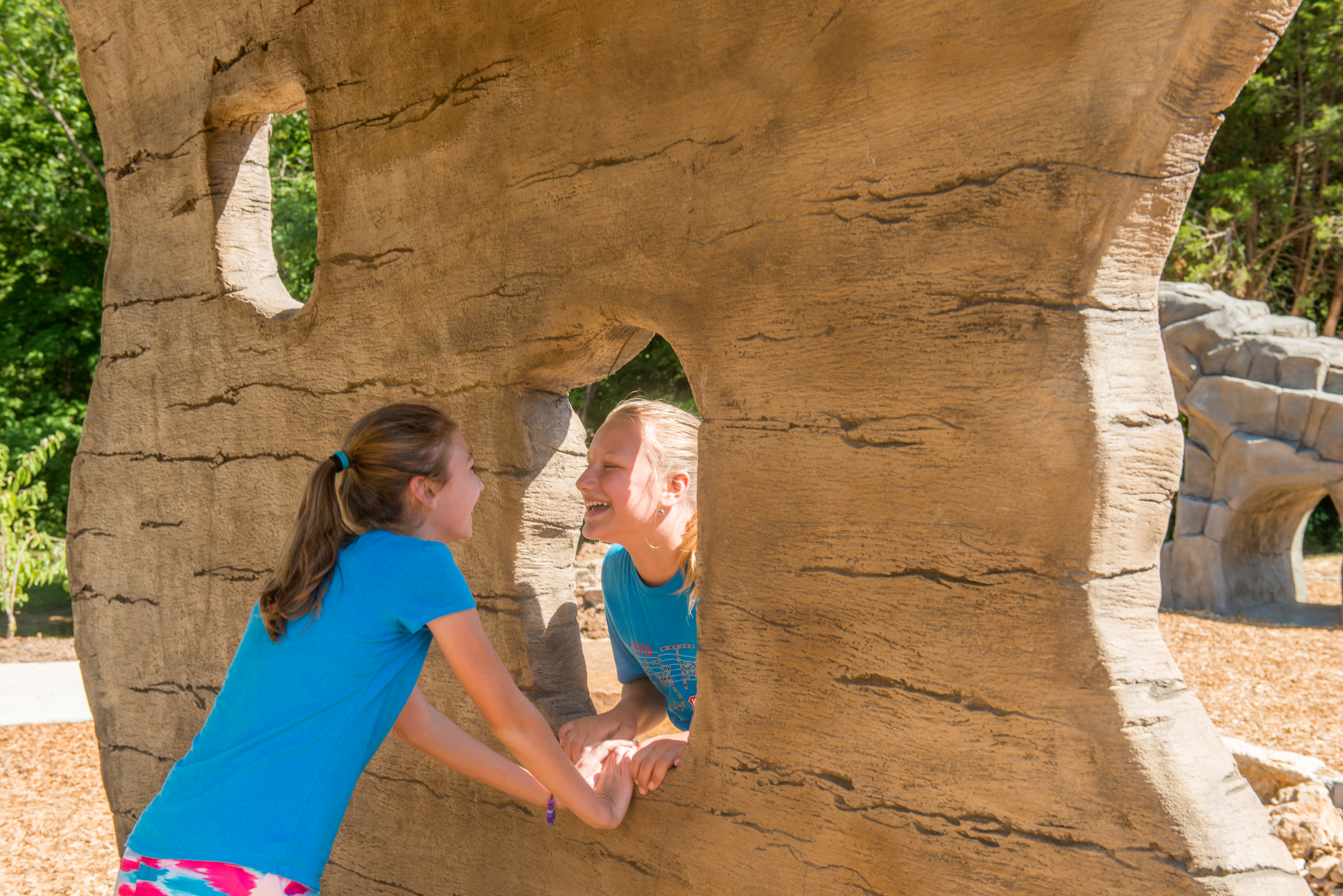 A tall thin rock with a hole in the middle with too girls looking at each other through the hole