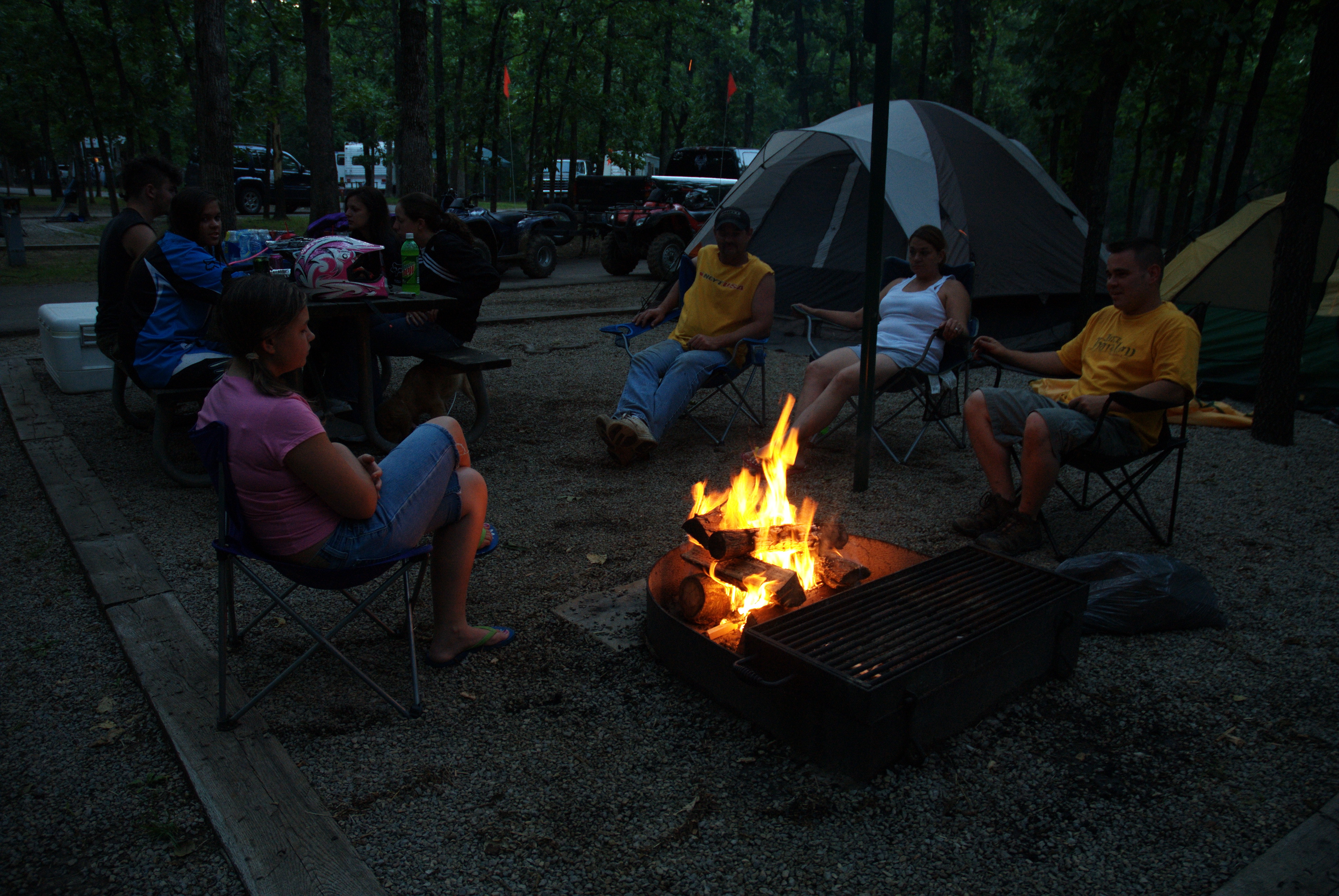 Eight campers sitting in lawn chairs around a fire