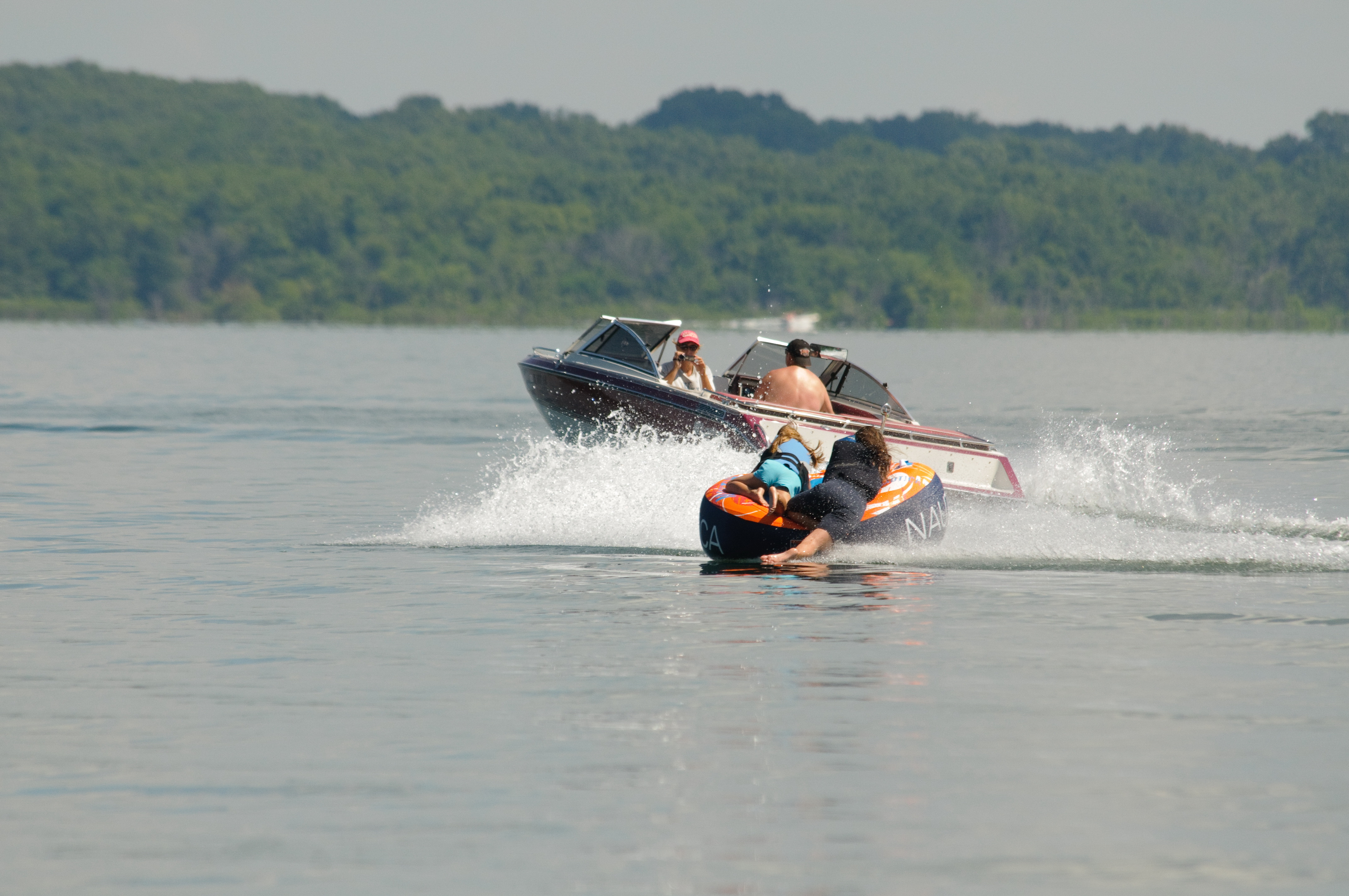 Two kids riding in an inflatable boat tied to a power boat