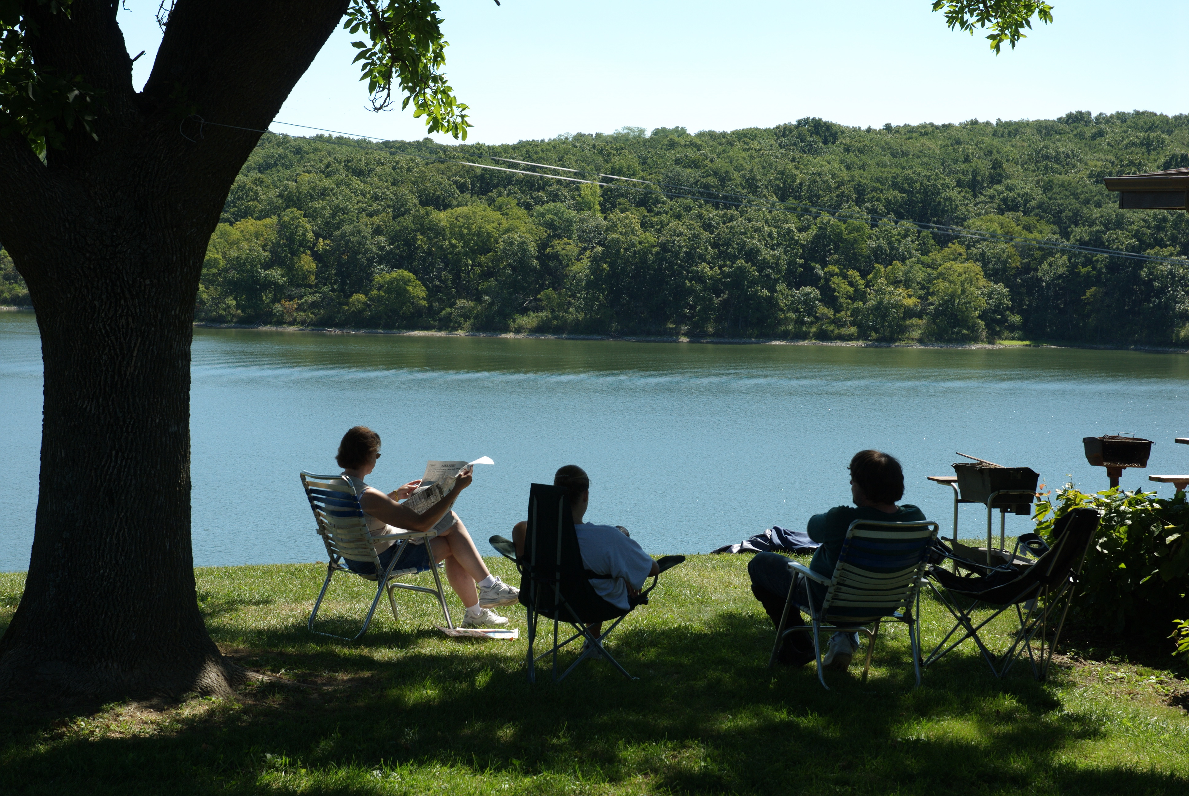 Three folks sitting on a hill over looking the water