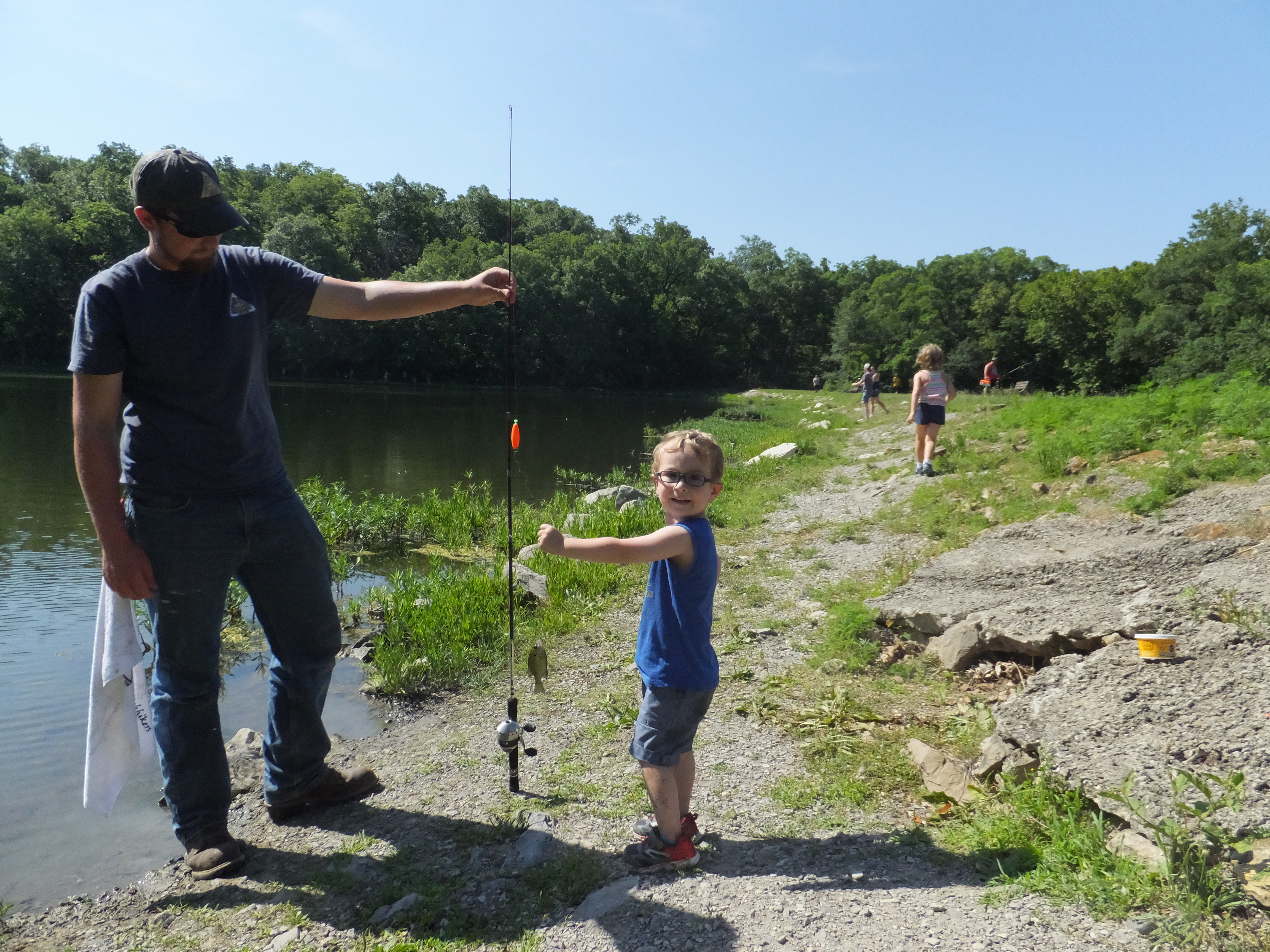 A man and a child with a fishing pole by the water