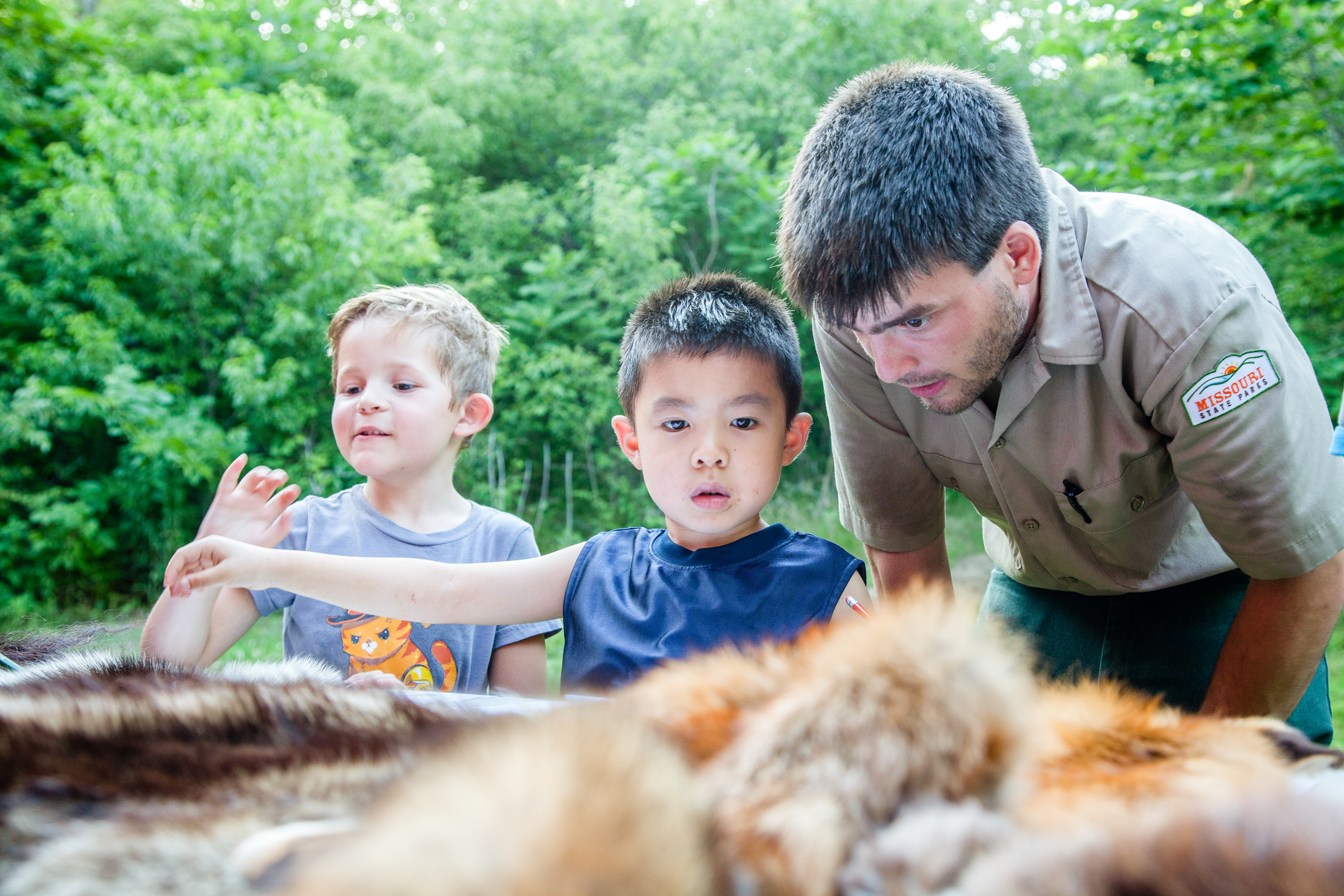 A man and two children examining animal pelts on a table