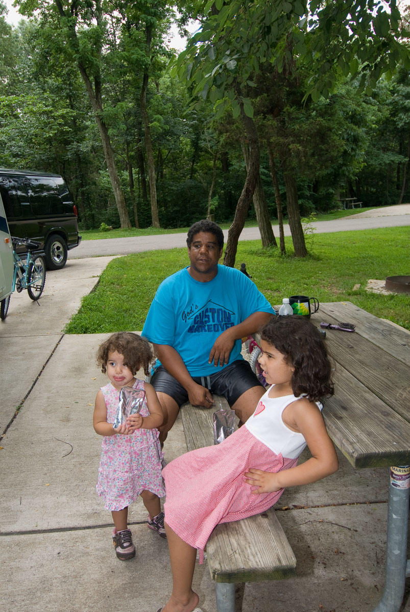 A family sitting at a picnic table outside a camper