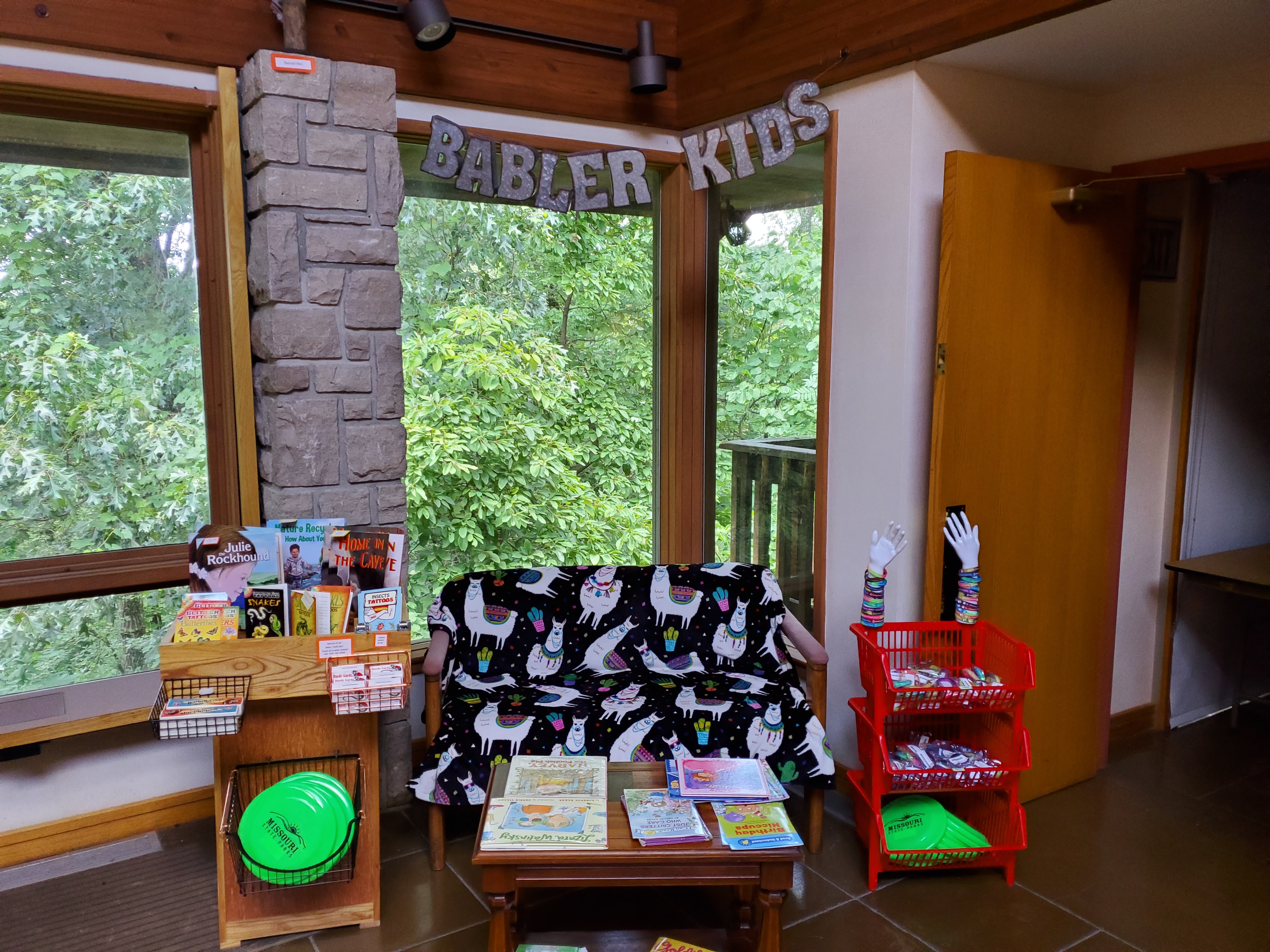 A couch and book shelf in a corner with "Babler Kids" on a sign above it