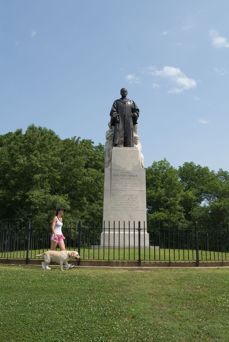 A woman walking a dog by the Dr. Edmund A. Babler Memorial Statue