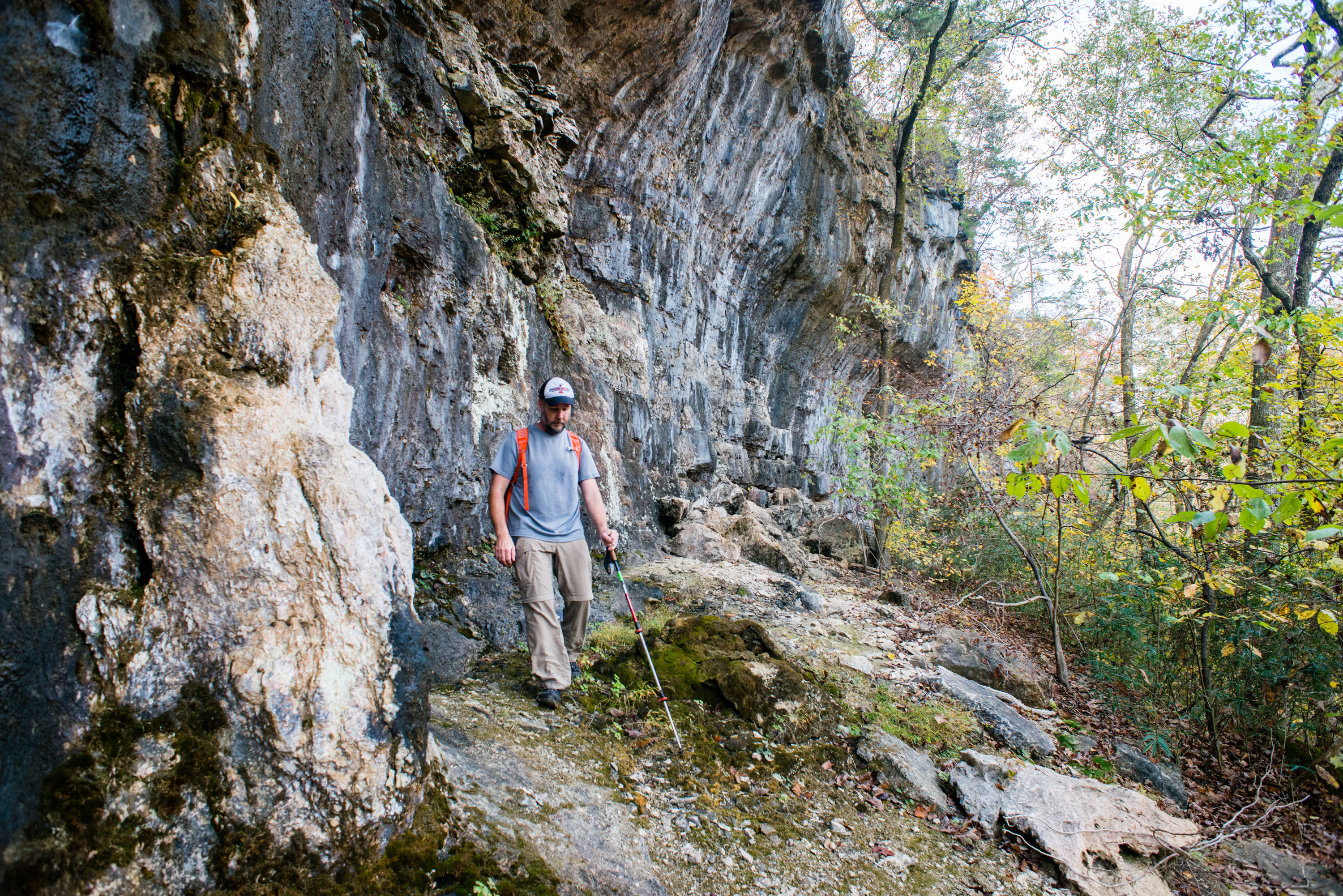 A man with a walking stick hiking on a narrow trail