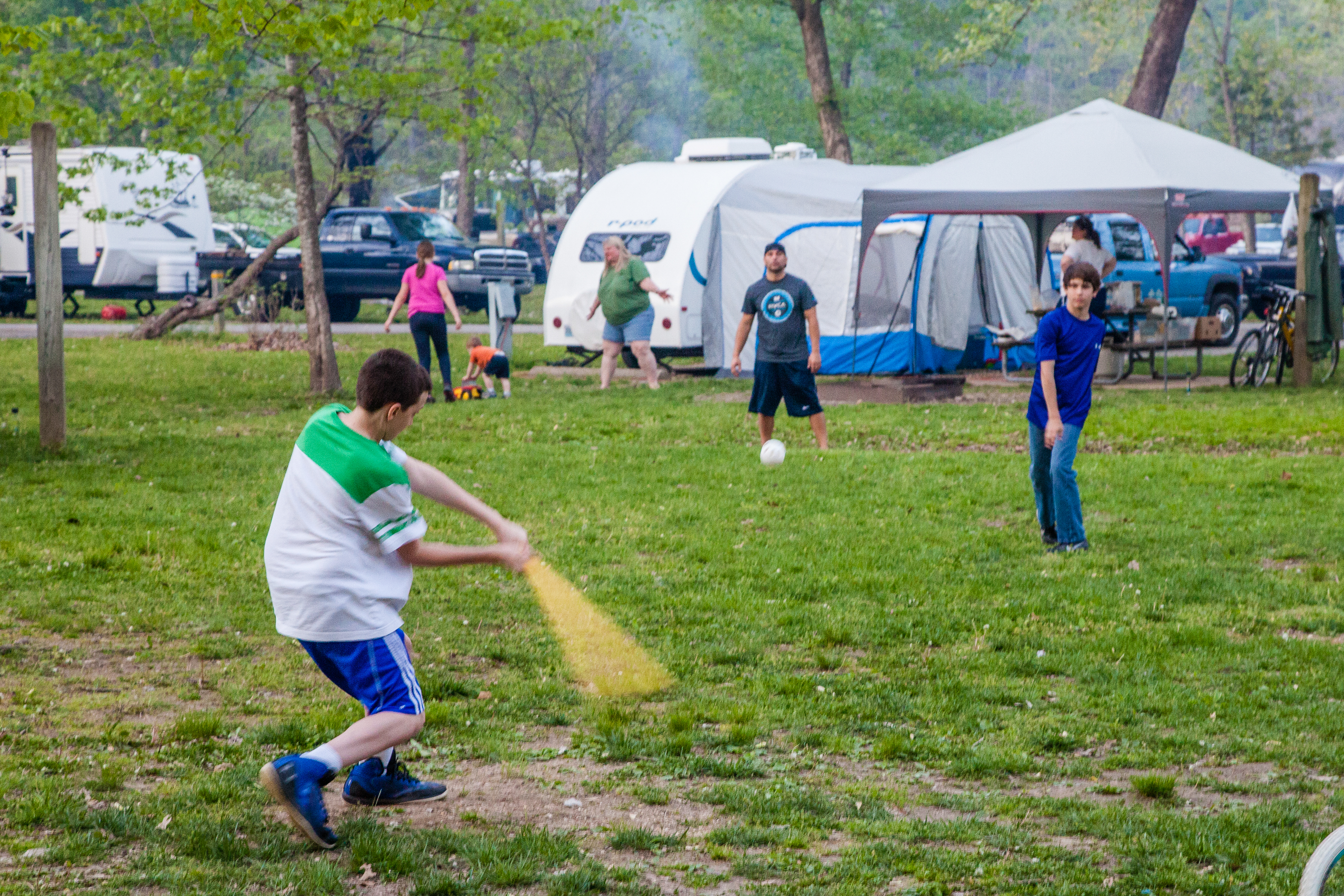 A group of people playing baseball outside a camper