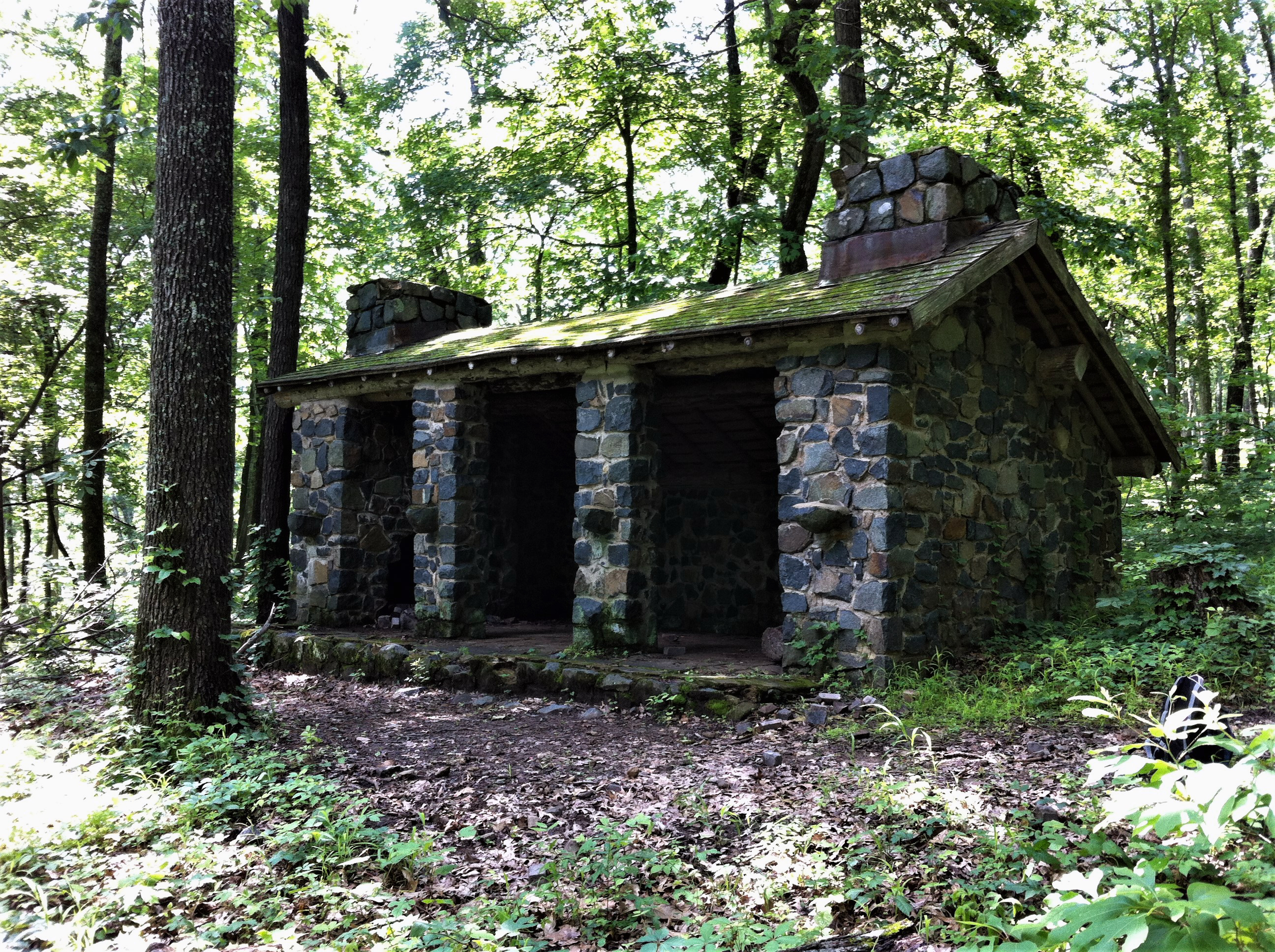 Large stone shelter along hiking path in woods.