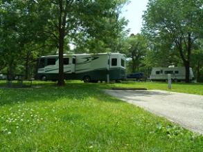 a long white camper backed into a shaded campsite
