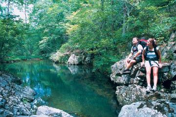 Backpackers sitting on rocks near water in the woods