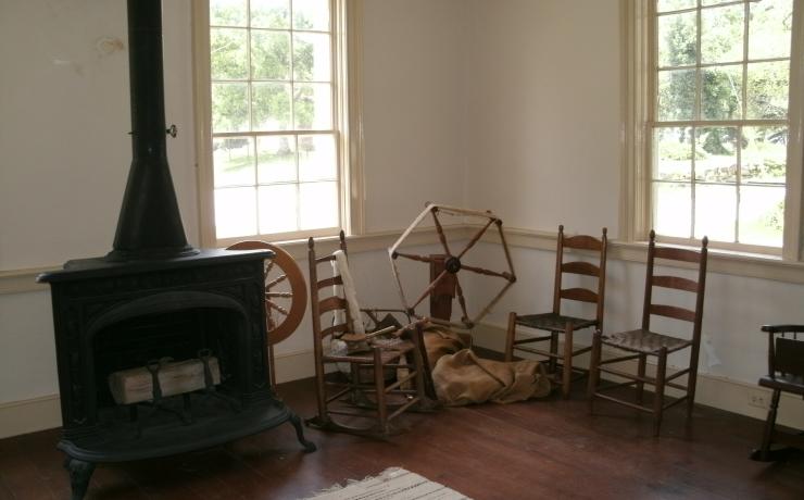 A colonial era living room with a wood burning stove and a spinning wheel