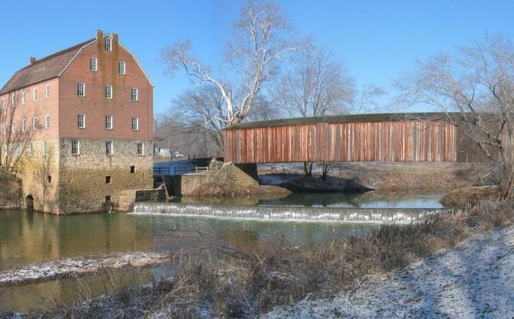 An old stone and brick mill next to a river with a covered bridge