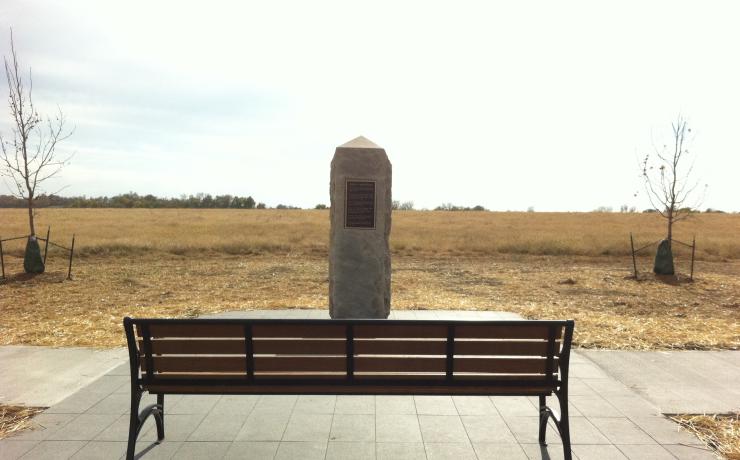 A wooden bench with a stone pillar monument in front of it