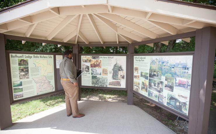 A man standing at a pavillion with three information signs about Bothwell