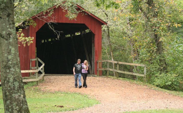 Two people standing in front of a red covered bridge