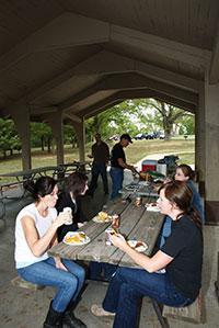 several people enjoying a meal under one of the picnic shelters