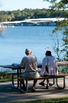 Two people sitting at a picnic table looking over a lake