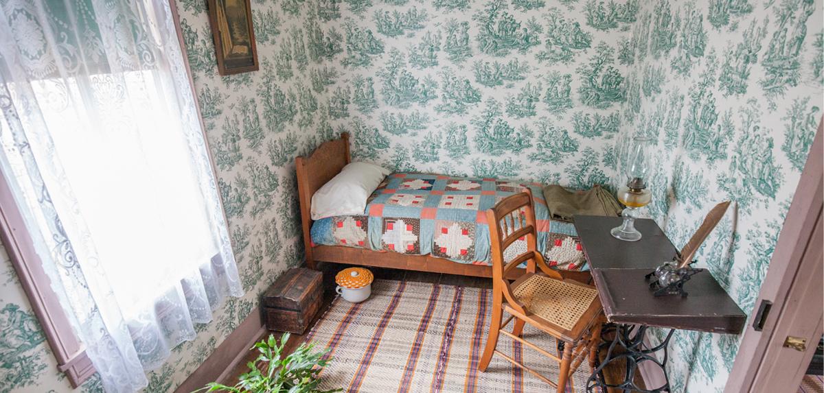 A small sunlit bedroom with bed, desk and chest