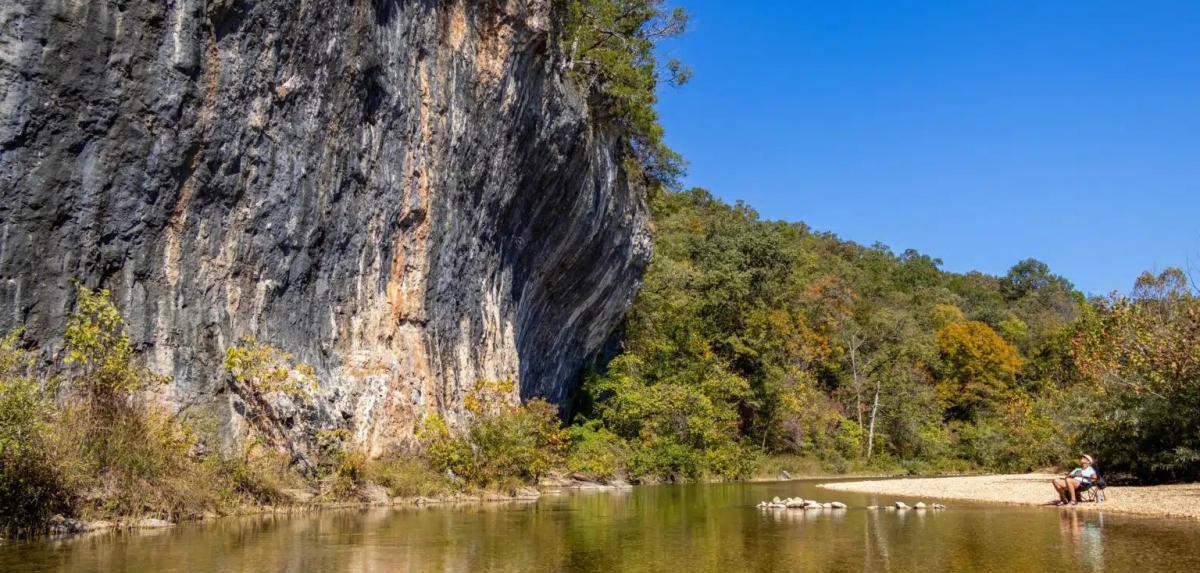 Woman looking up at a bluff from a lawn chair on a creek bank