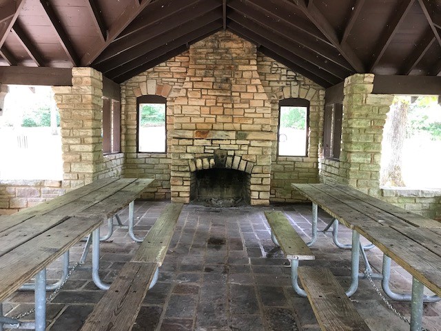Interior of shelter, with stone floor and fireplace and wooden picnic tables