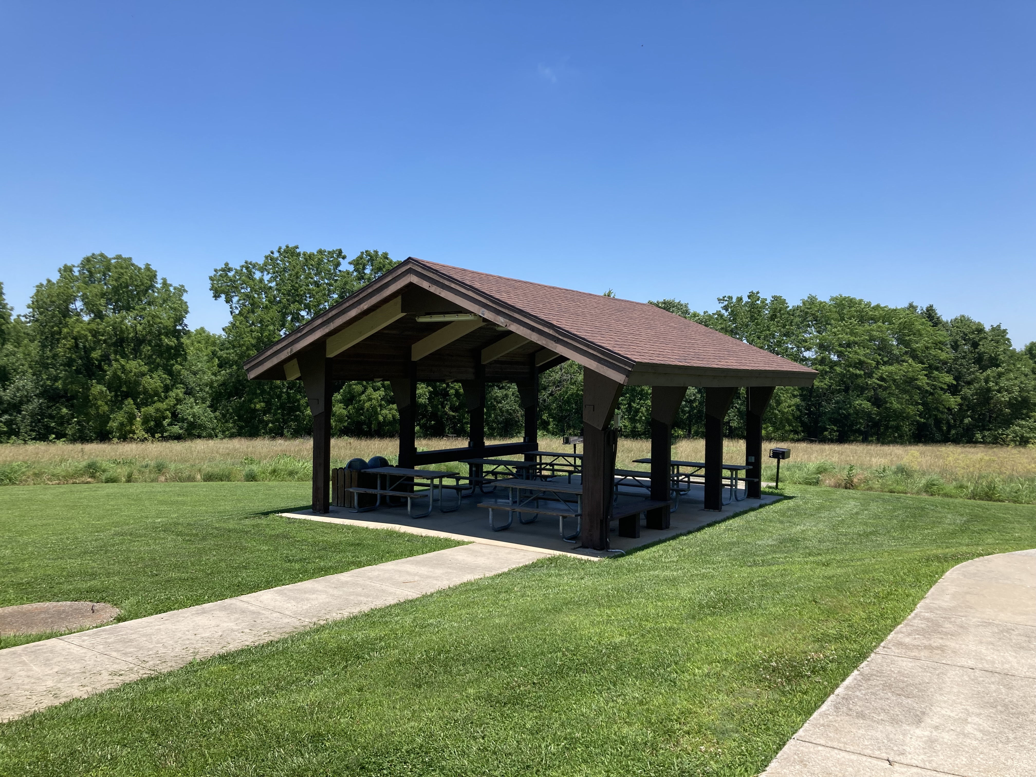 Open picnic shelter with roof and six picnic tables and a pedestal grill