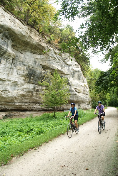 two bicyclists riding on the trail next to a bluff
