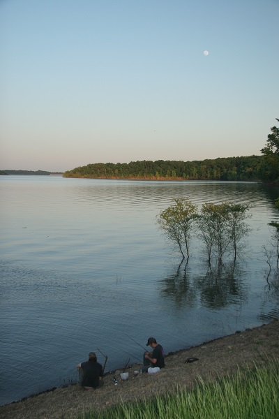 two people sitting on the bank of the lake at dusk