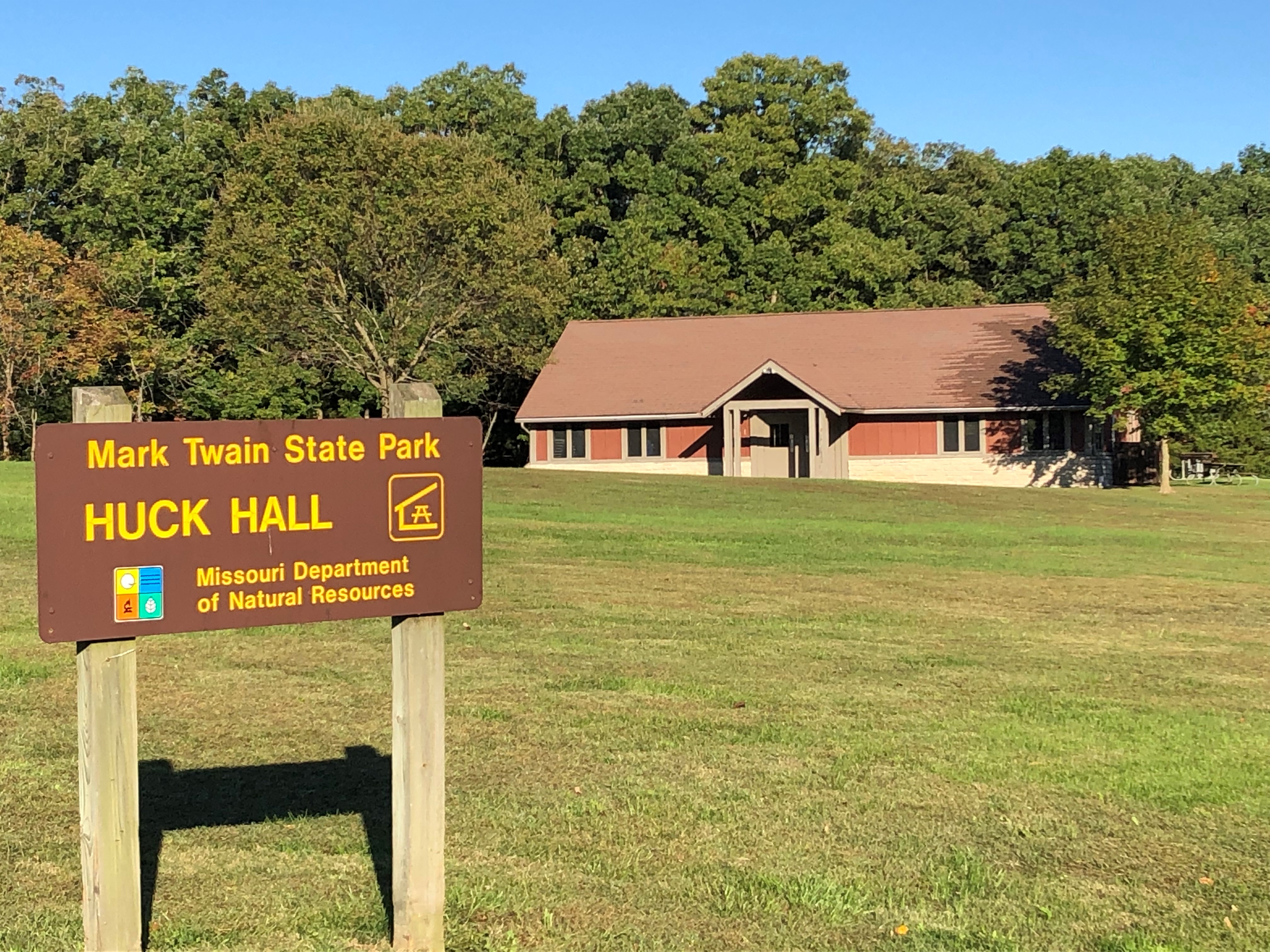Sign for Huck Hall, with the enclosed shelter in the background, across a field