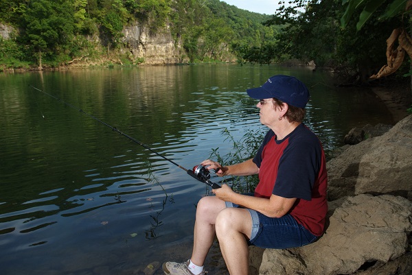 a man sitting on a rock on the shore fishing in the river