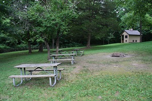 three picnic tables in an open area with a vault toilet in the background