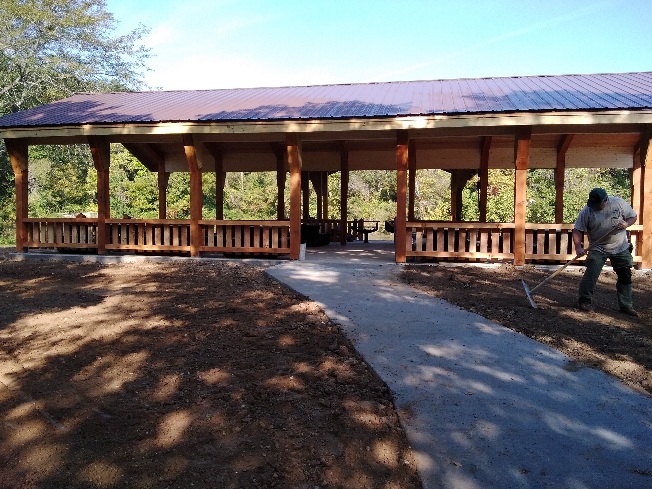 Worker raking dirt in front of the open picnic shelter