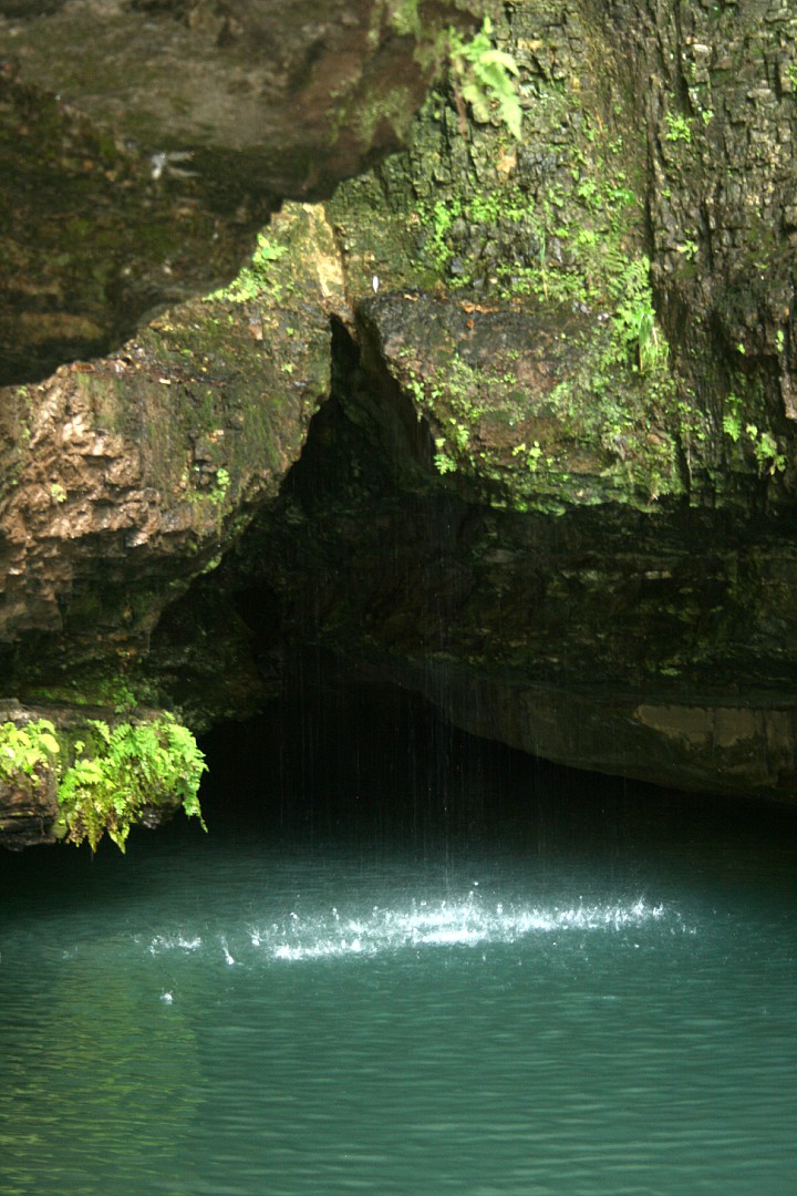 blue sping water below moss-covered rock opening with water dripping down