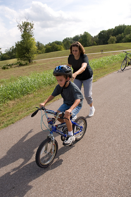 woman helping a child learn to ride a bike
