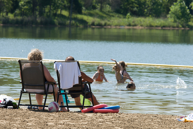 two people sitting in lawn chairs on the beach watching kids swim